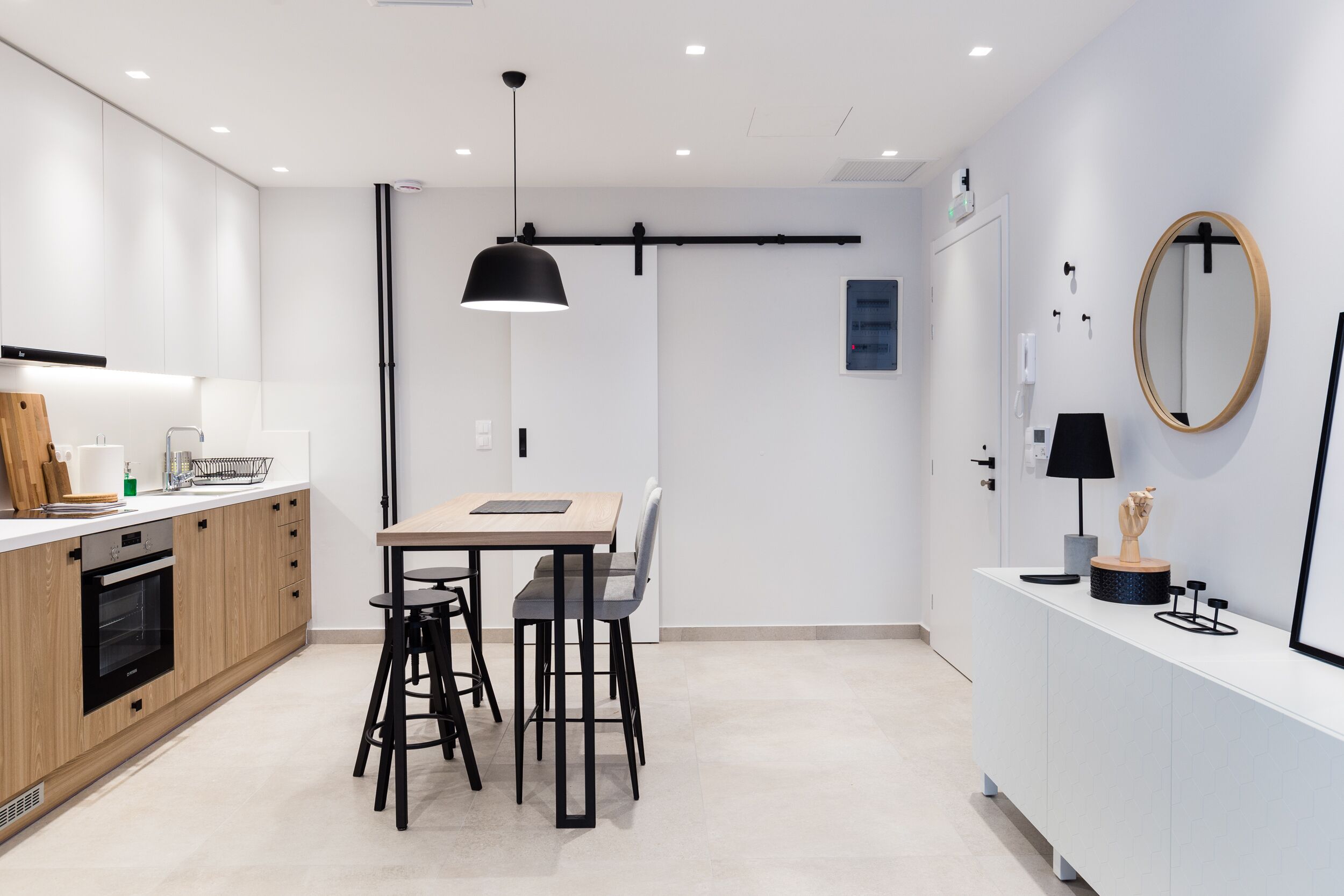Uma cozinha moderna com área de refeições, com bancada de madeira, luminárias pendentes pretas e um armário branco com espelho.