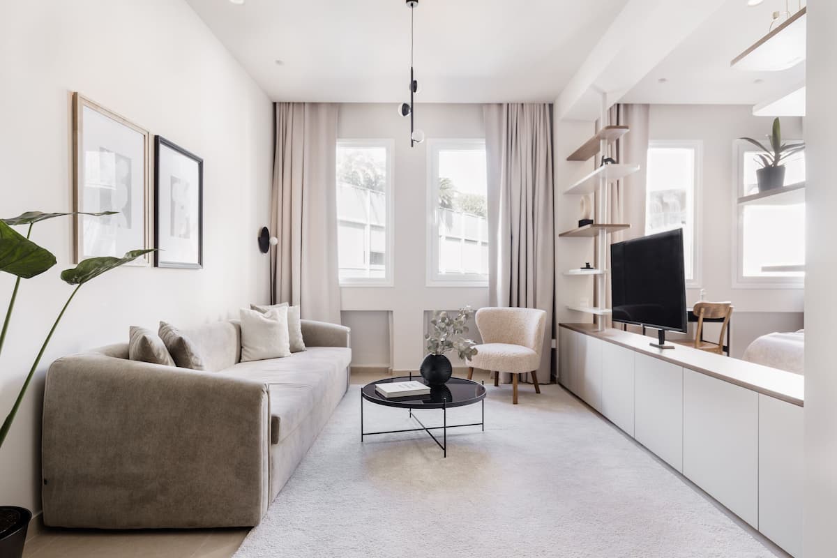 A modern living room with a sofa, armchair, coffee table, TV, and shelves.