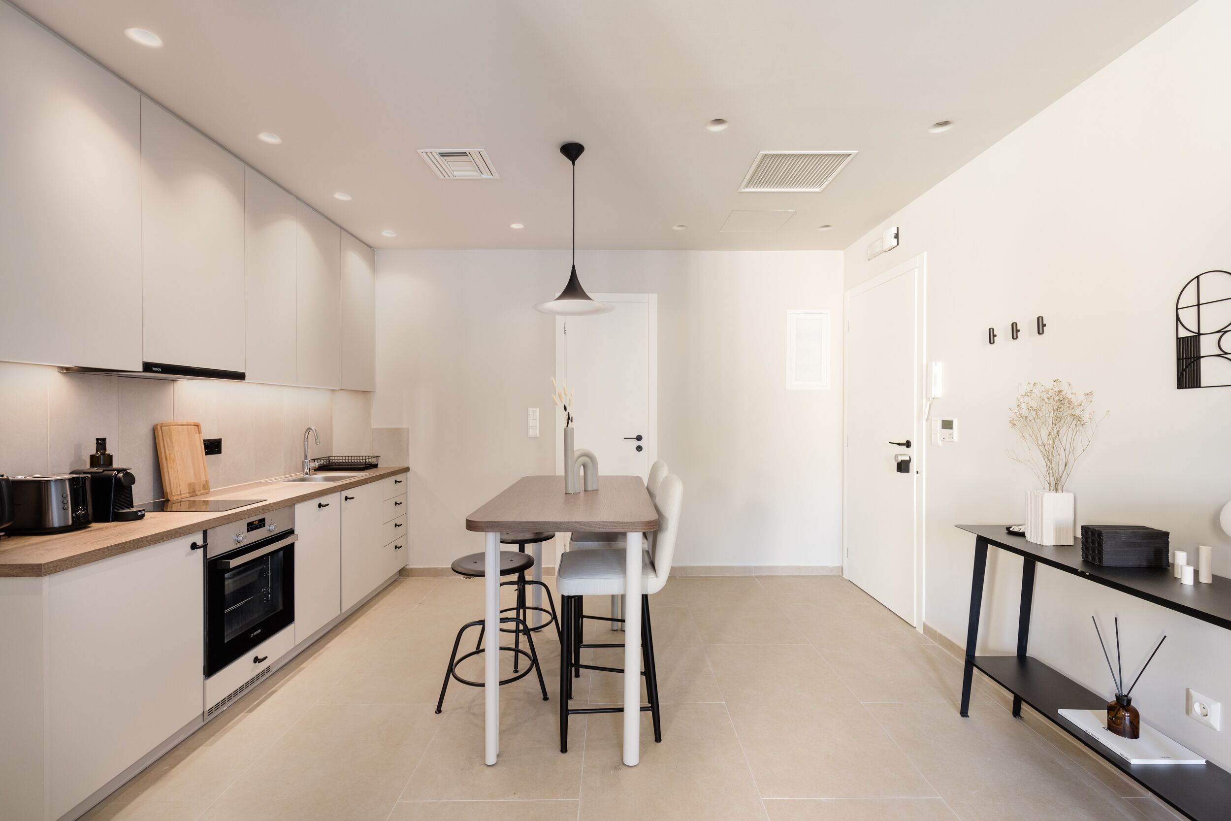 Une cuisine moderne avec des meubles blancs, un four encastré et un coin repas comprenant une table et des chaises.