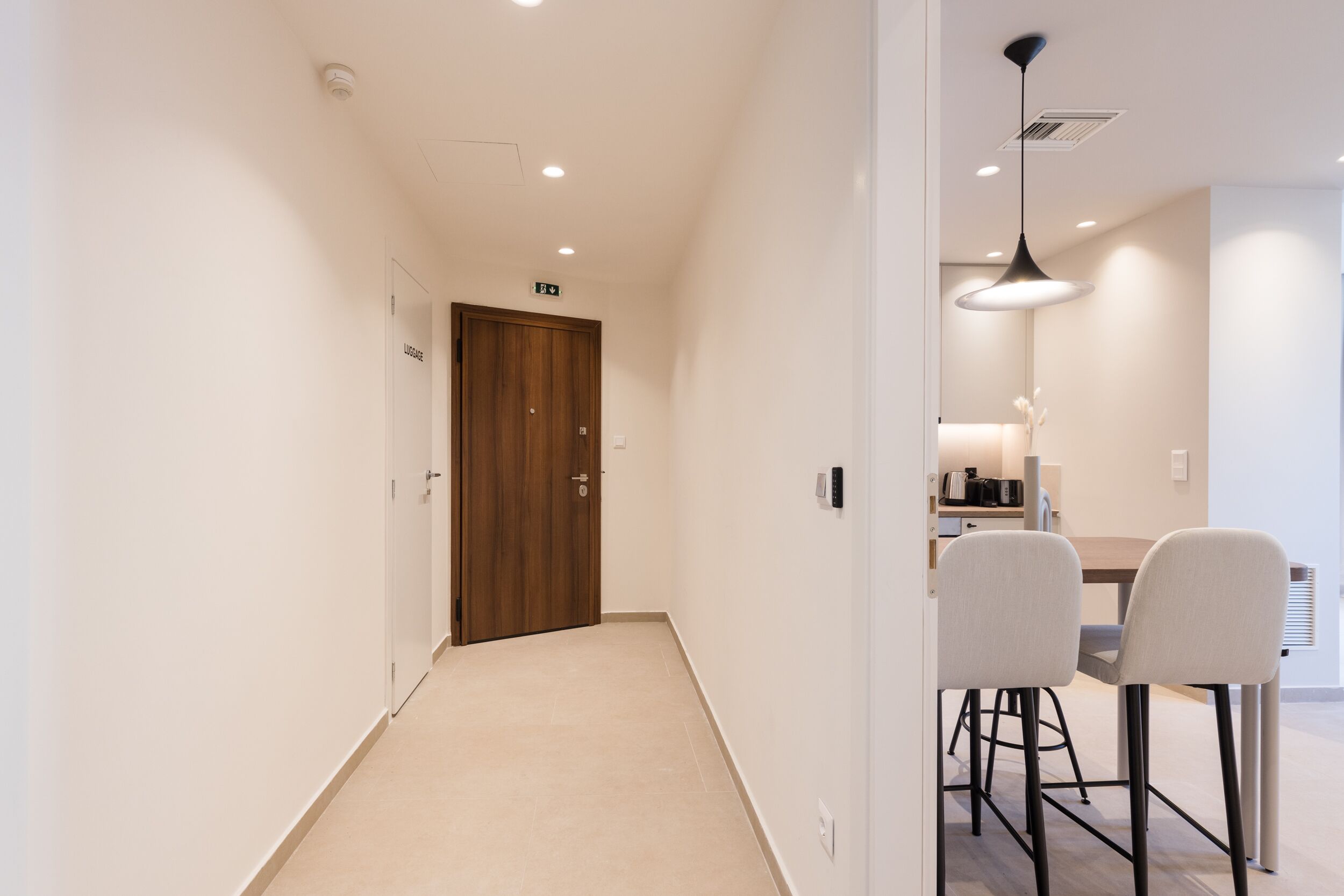 A hallway leading to a dining area with a wooden door, a ceiling light, and a table with chairs.