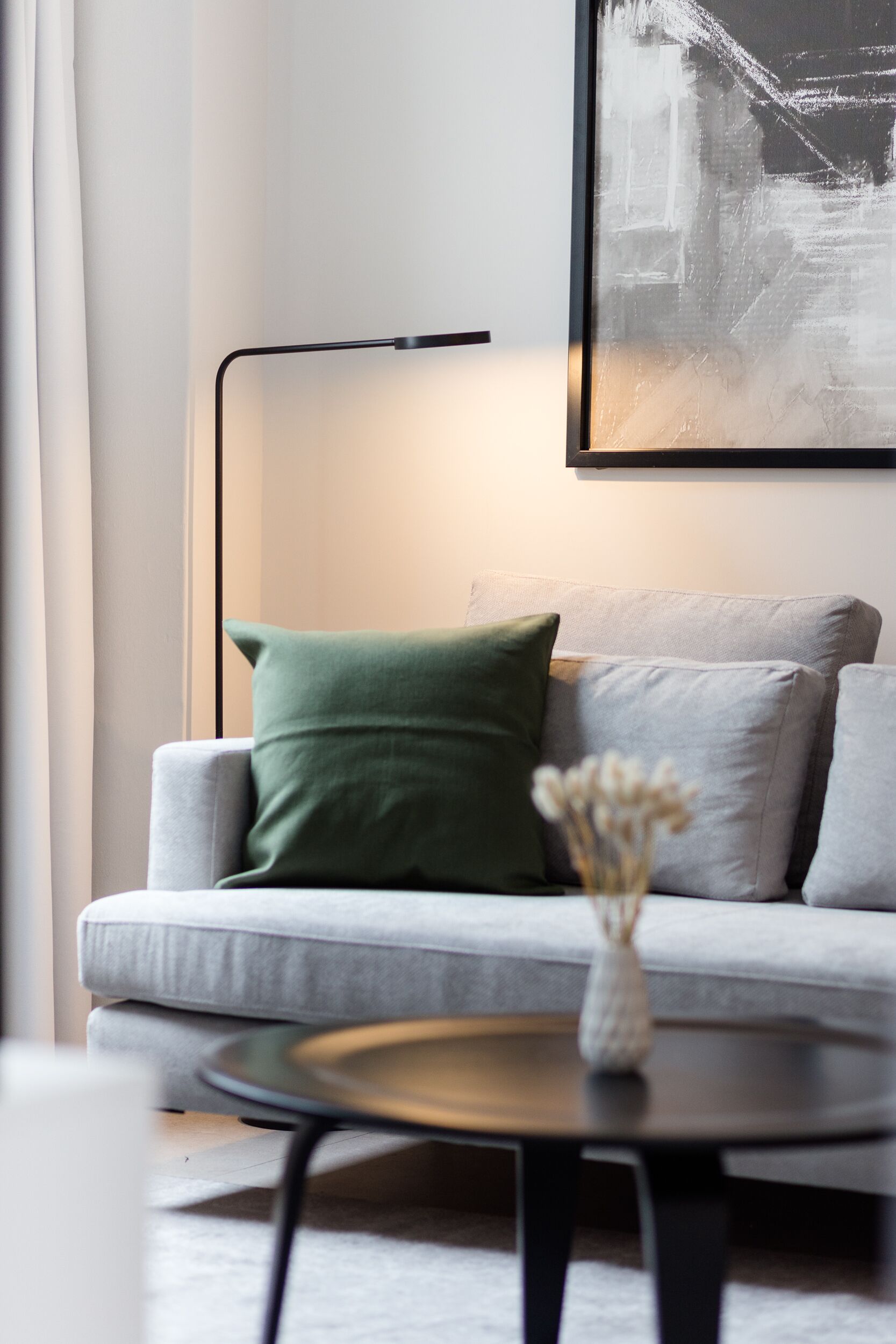 A modern living room with a grey sofa, a green pillow, a vase with flowers, and a floor lamp.