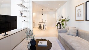 A modern living room with a flat-screen TV, a round coffee table with a book, a sofa, and a dining area with a table and chairs. - UPSTREET Luxury Apartments in Plaka (Athens)