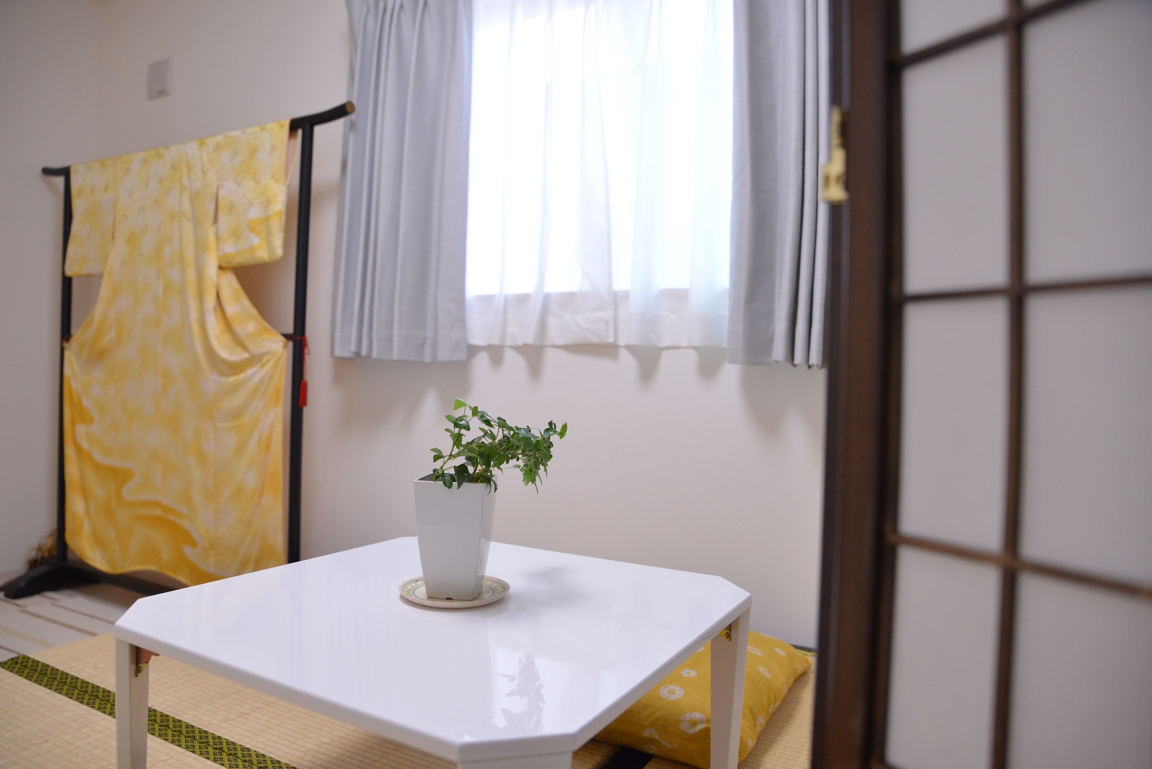 Une pièce avec une table blanche, une plante en pot, une serviette jaune et une fenêtre avec des rideaux.