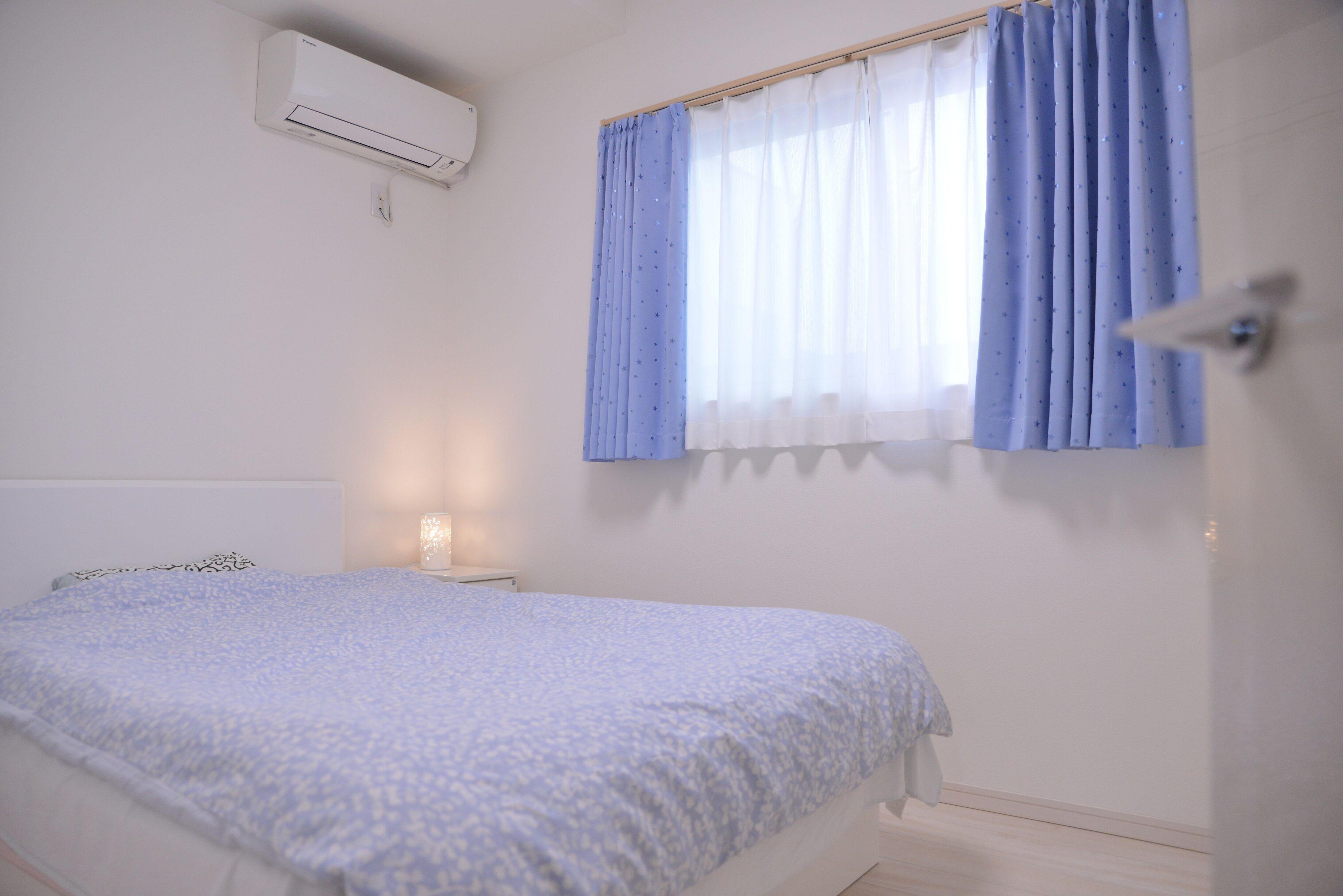 A bedroom with a bed, a nightstand, a wall-mounted air conditioner, and a window with curtains.