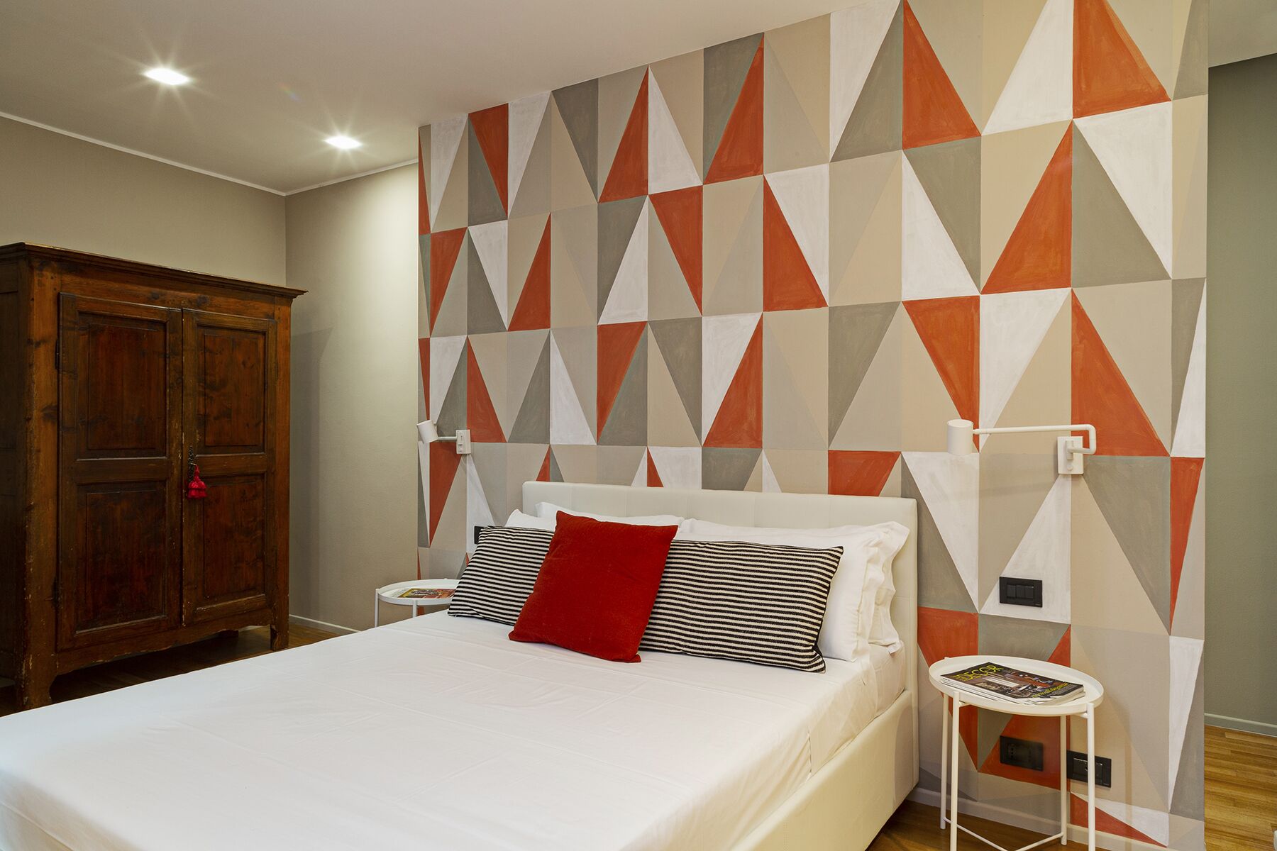 Una camera da letto con un letto, un armadio in legno e una parete con motivo geometrico.