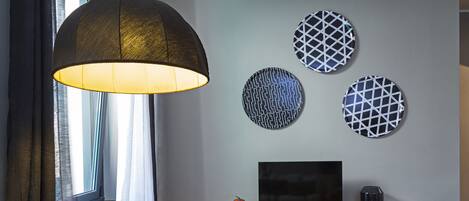 A modern living room with a leather armchair, a large pendant lamp, a flat-screen TV, and decorative wall art.