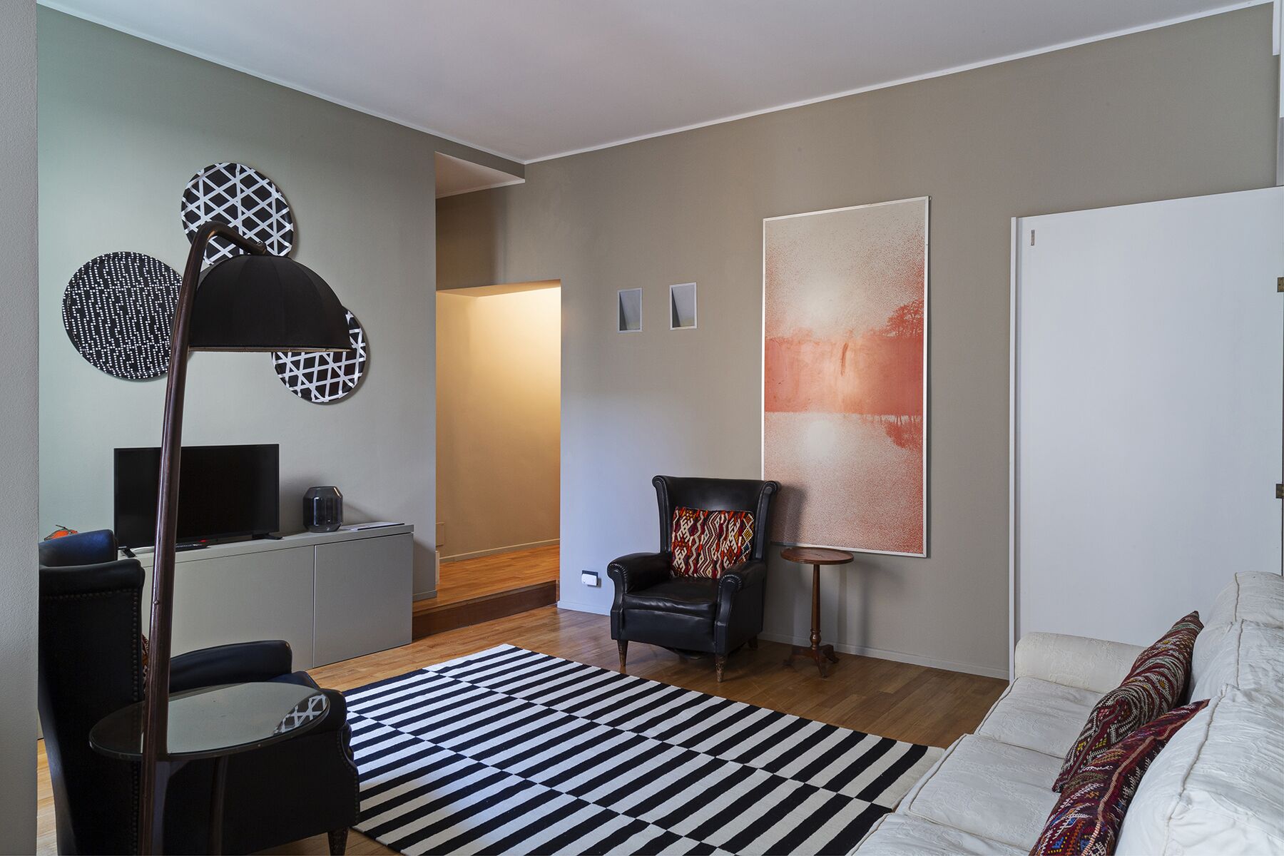 Een moderne woonkamer met een zwarte lederen fauteuil, een zwart-wit gestreept vloerkleed, een flatscreen televisie en een groot abstract schilderij aan de muur.