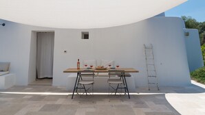 Un área de comedor al aire libre con una mesa, dos sillas, una escalera y una pared blanca.