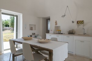 A modern kitchen with white cabinets, a dining table with chairs, and a large window.