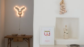 Una habitación con una mesa de madera, un cartel de bienvenida enmarcado, un diente de ajo colgando y una botella en un estante.
