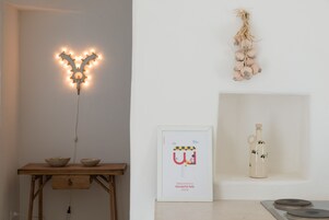 A room with a wooden table, a framed welcome sign, a hanging garlic bulb, and a bottle on a shelf.