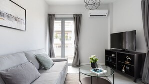 A modern living room with a sofa, a glass coffee table, a TV, and a bookshelf. - UPSTREET Minimal 2BD Apt-Lycabettus view (Kaisariani)