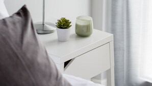 A neatly made bed with a grey pillow, a white bedside table with a lamp, a small potted plant, and a green candle. - UPSTREET Minimal 2BD Apt-Lycabettus view (Kaisariani)