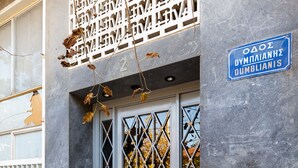 A building with a blue sign reading "OAO OUMPLIANNE OUMBLIANIS" and a metal gate with a diamond pattern. - UPSTREET Minimal 2BD Apt-Lycabettus view (Kaisariani)