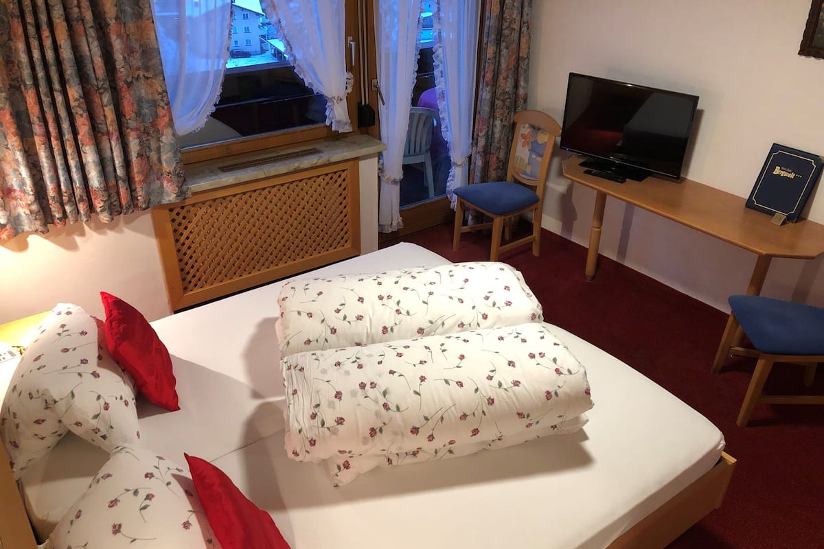A hotel room with a bed, a desk with a TV, and a chair.