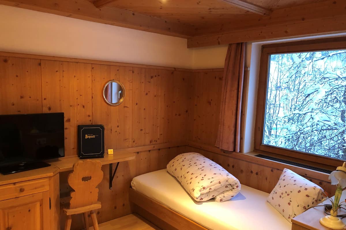 A cozy cabin room with a bed, a television, a mirror, and a window with a view of trees.