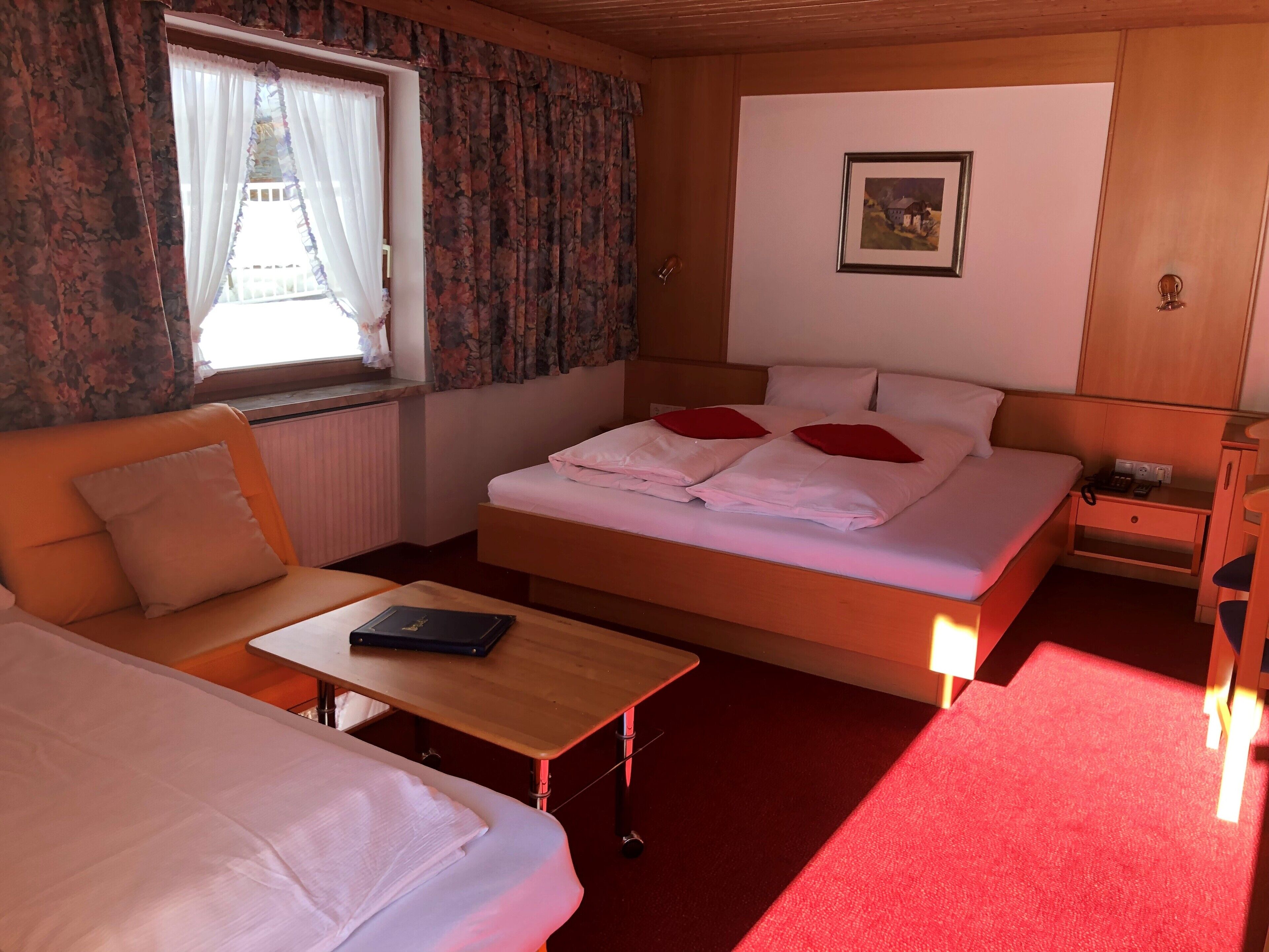 A hotel room with a bed, a sofa, a table, and a window with curtains.