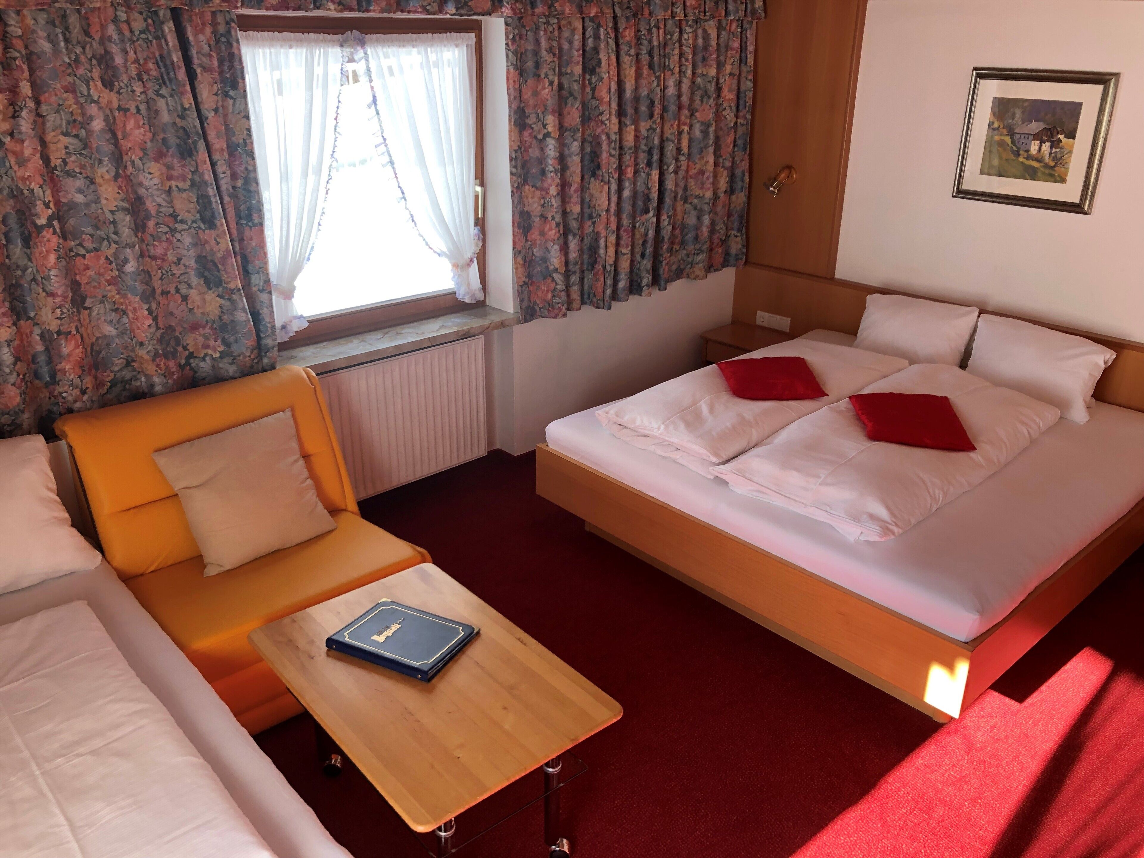 A hotel room with a bed, a sofa, a small table, and a window with curtains.