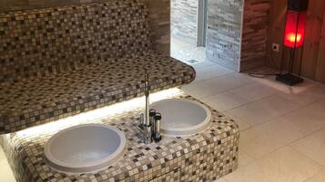 Relax in a spacious bathroom with a unique tiled design, featuring a large sink with two basins and a curved bench for seating.