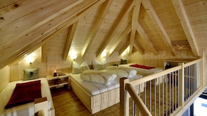 A wooden cabin with a loft bedroom featuring a bed, a desk, and a red blanket. - Hotel Garni Bergwelt (See)