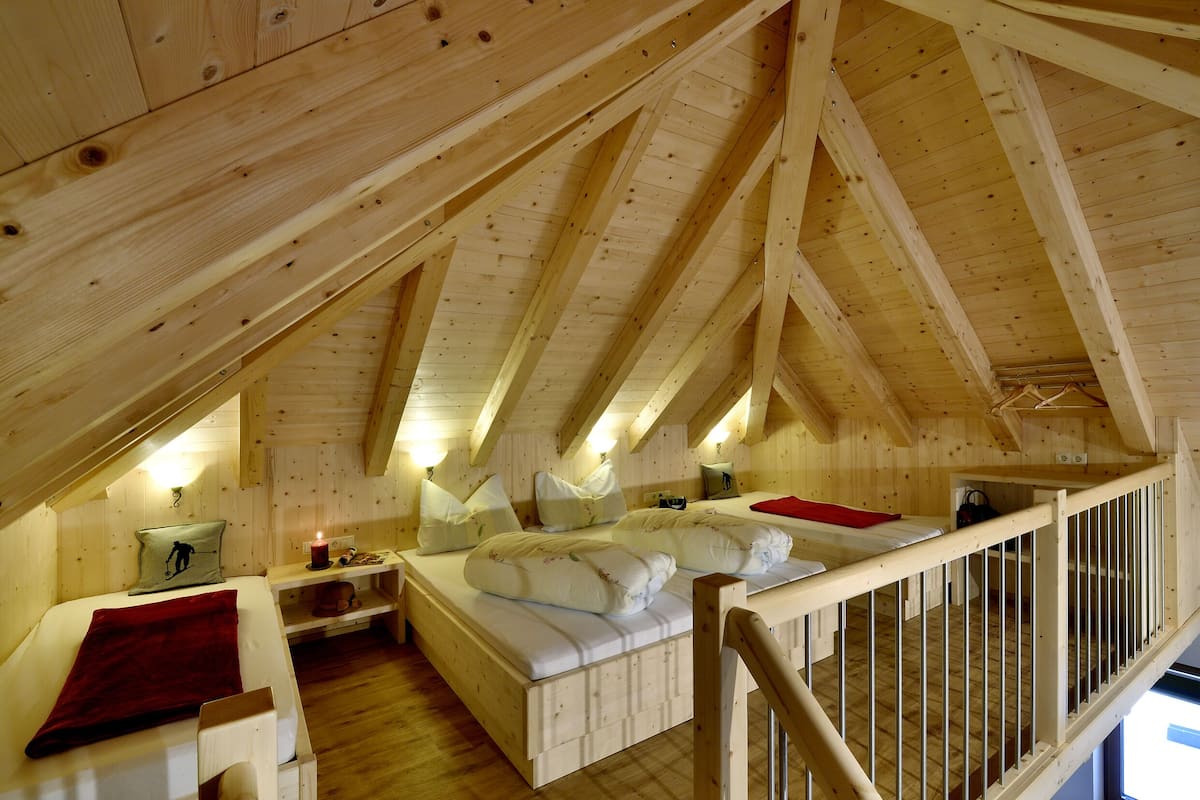 A wooden cabin with a loft bedroom featuring a bed, a desk, and a red blanket.