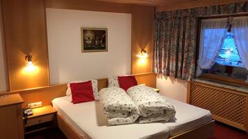 Una habitación de hotel con cama, dos mesitas de noche, una lámpara de pared, ventana con cortinas e imagen enmarcada en la pared.