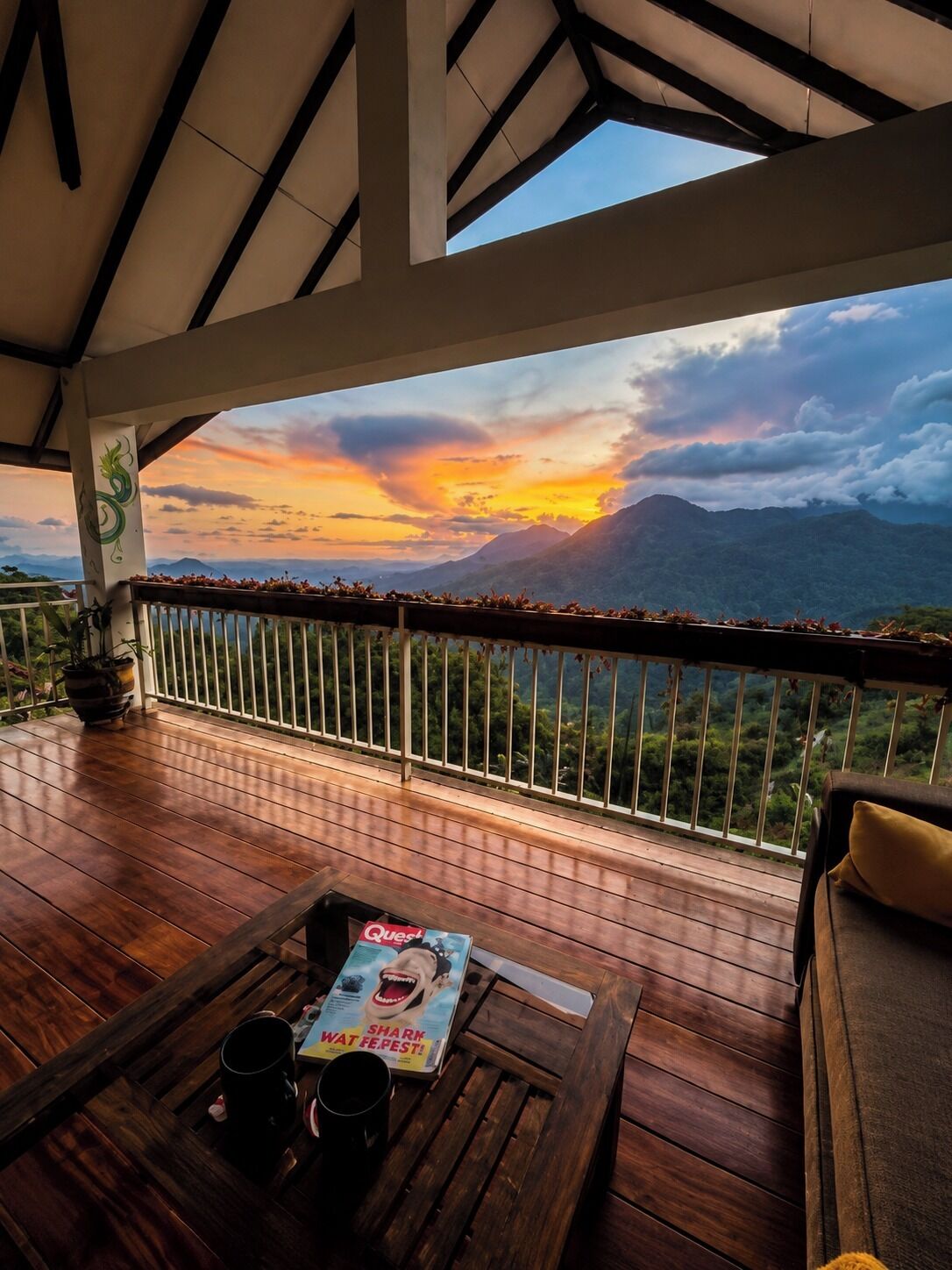 A wooden deck with a view of mountains and a sunset.