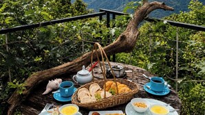 Ein Picknick auf einer Holzplattform mit Blick auf eine schöne Berglandschaft, inklusive Korb mit Brot, Tellern mit Essen und einem Teekessel.