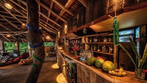 Eine rustikale Bar mit Holzböden, Regalen voller Flaschen, einer Holztheke und einer hängenden Leuchte.