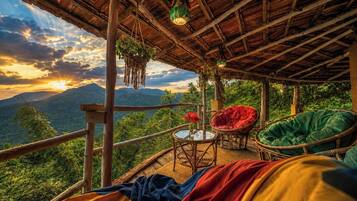 A wooden deck with wicker furniture, a glass table, and a view of mountains.