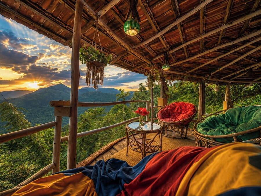 A wooden deck with wicker furniture, a glass table, and a view of mountains.
