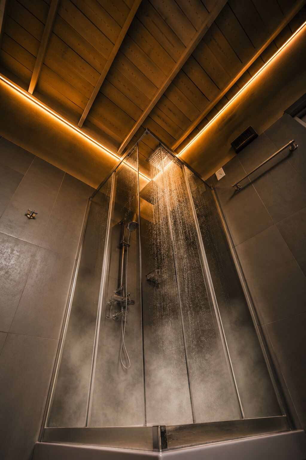 Um chuveiro moderno com divisória de vidro, iluminação embutida e teto de madeira.