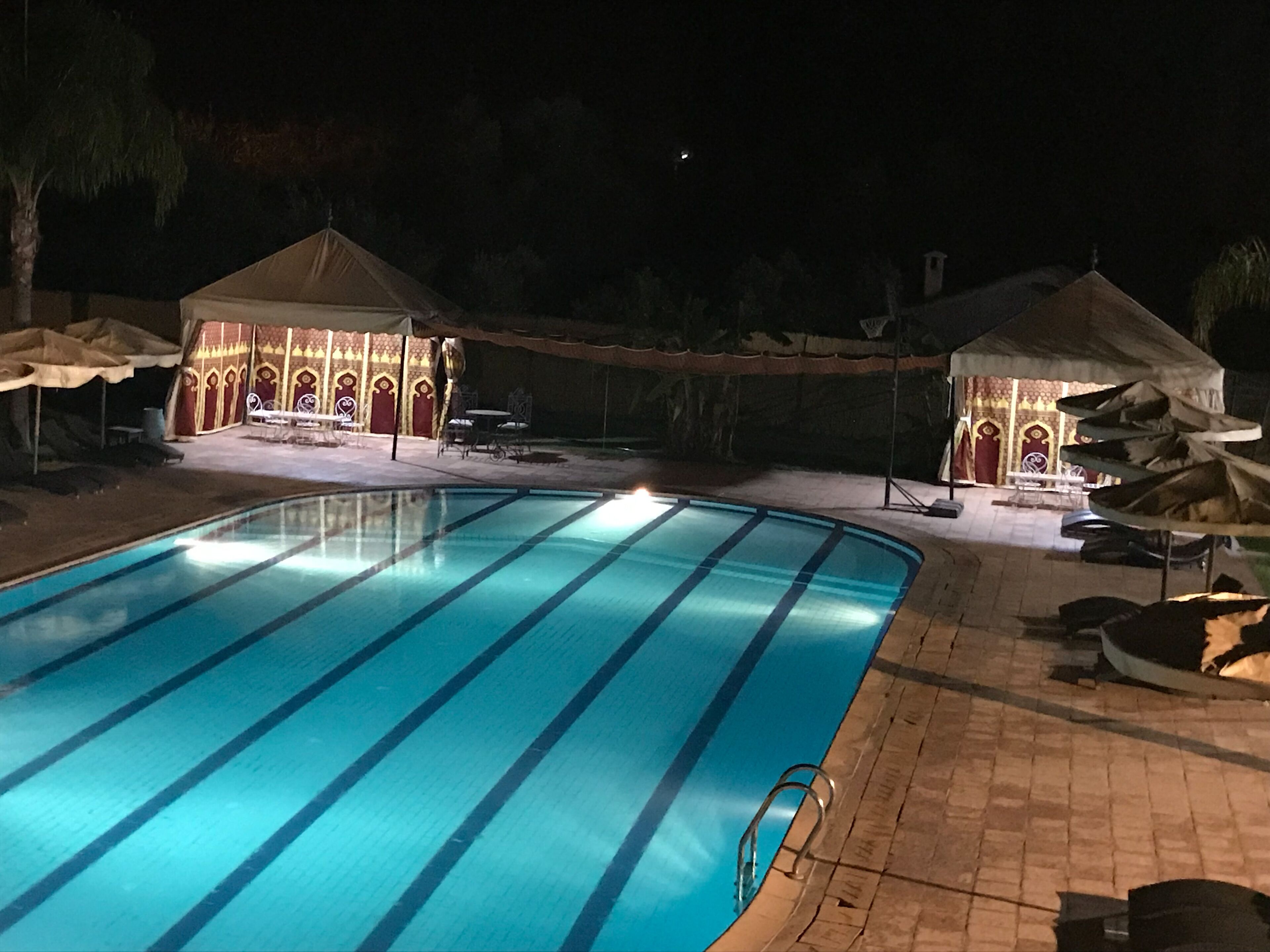 A swimming pool with a tiled deck, surrounded by lounge chairs and umbrellas.