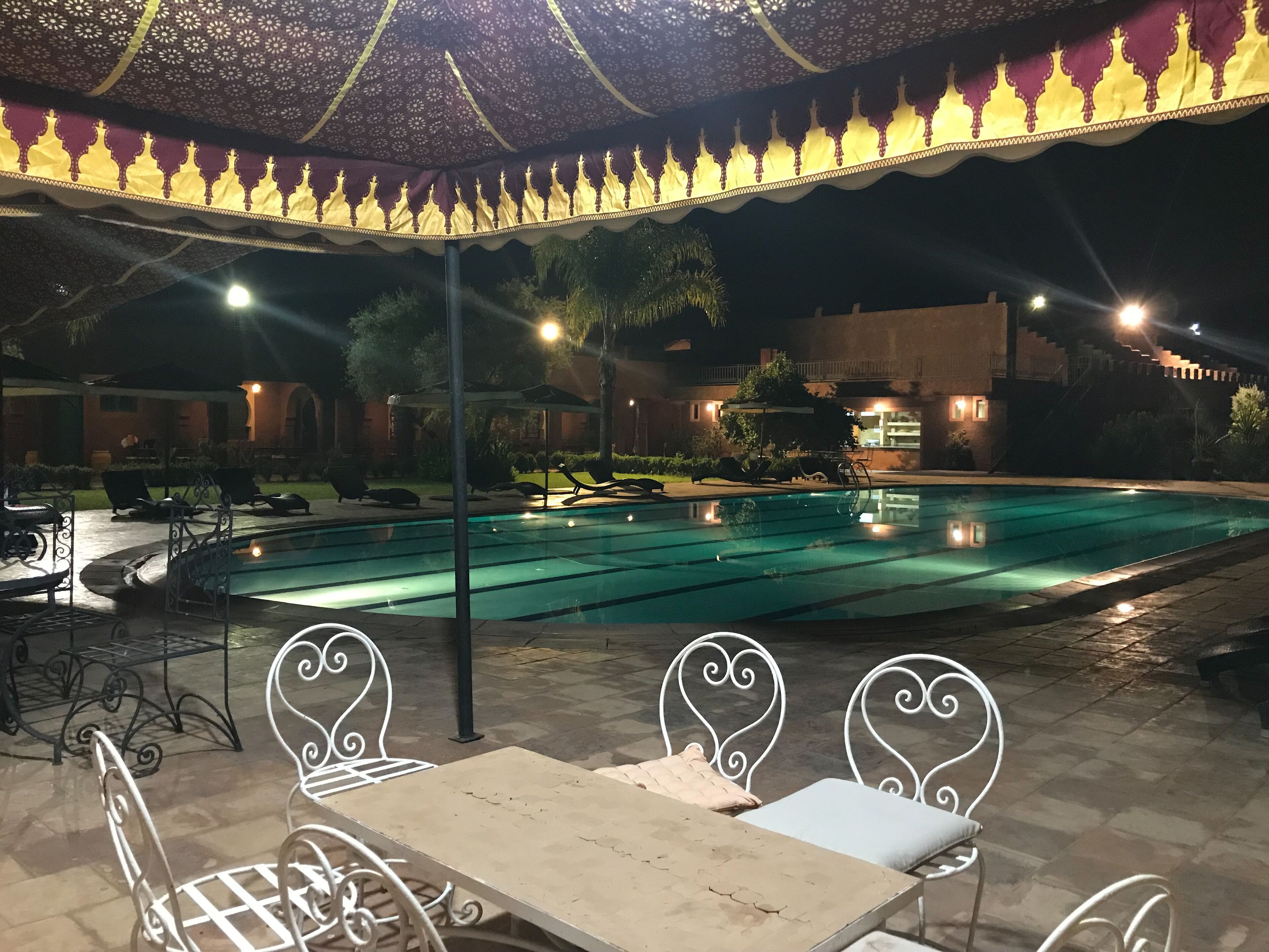 An outdoor pool area with lounge chairs and tables, surrounded by a decorative canopy.