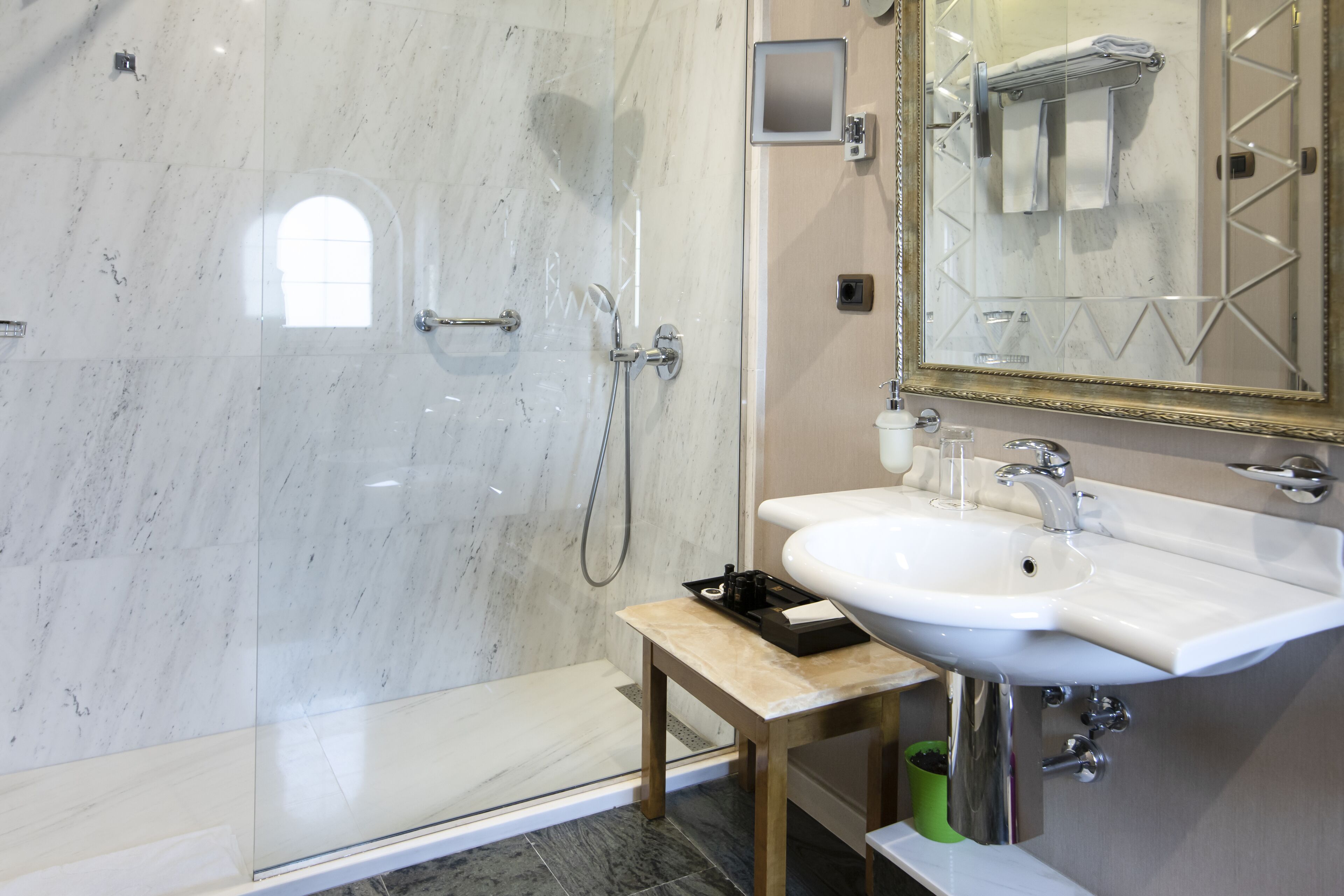 A modern bathroom with a glass-enclosed shower, a sink with a mirror, and a small table with toiletries.