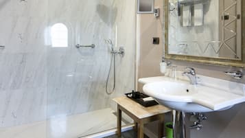 A modern bathroom with a glass-enclosed shower, a sink with a mirror, and a small table with toiletries.
