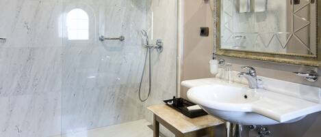 Un baño moderno con ducha de vidrio, lavamanos con espejo y una mesita con artículos de aseo.