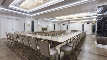 Un salón de conferencias con una larga mesa, sillas y una araña.