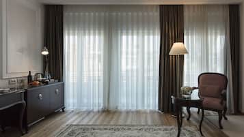 Habitación de hotel con piso de madera, un sofá de color oscuro, una mesita de noche con lámpara, un florero de vidrio con flores y un aparador oscuro.