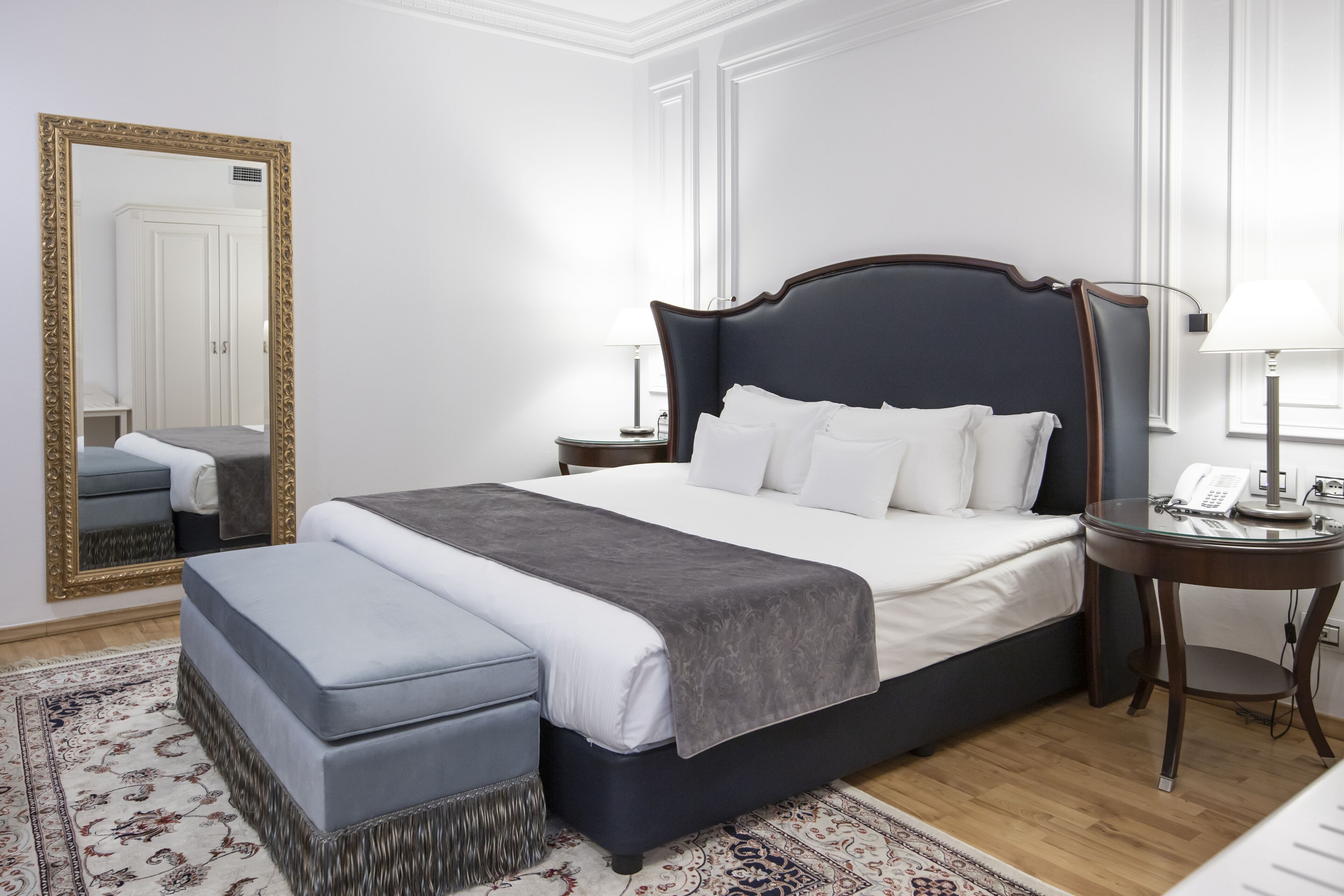 A neatly arranged bedroom with a large bed, bedside tables, a mirror, and a patterned rug.