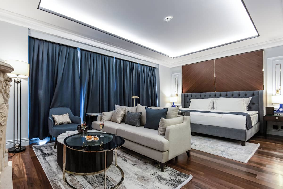 Et moderne hotelværelse med sofa, rundt sofabord, seng og stort vindue med gardiner.