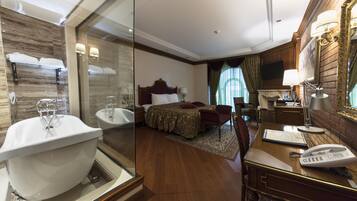 A hotel room with a large bathtub, a bed with a headboard, a desk with a telephone, and a television.