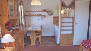 A compact kitchen with wooden cabinets, a dining table, and a small refrigerator. - 2-room apartment, ski-in/ski-out, pets allowed (Méribel)