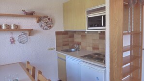 A compact kitchen with a microwave, stove, and dishwasher. There is a wooden table with chairs and a small shelf with decorative items. - 2-room apartment, ski-in/ski-out, pets allowed (Méribel)
