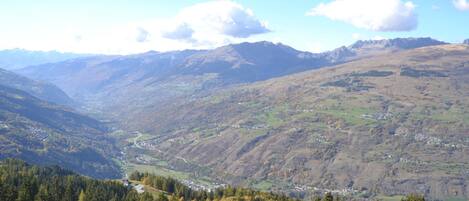 A mountainous landscape with a valley, dense forests, and distant mountains.