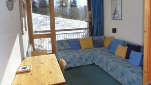 Une pièce chaleureuse avec une table en bois, un canapé bleu à motifs et une grande fenêtre donnant sur un paysage enneigé.