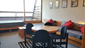 Una zona de estar acogedora con sofá, una mesa redonda y sillas. Se ve una ventana con vistas al exterior.