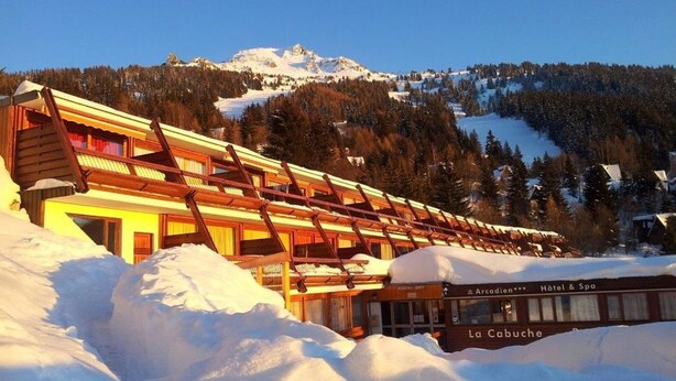 Un hotel cubierto de nieve con fachada de madera y un cartel que dice "Arcaden Hotel & Spa La Cabuche".