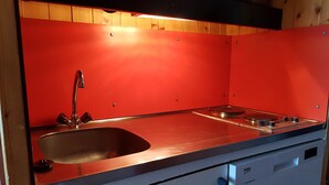 Una cocina con salpicadero rojo, pileta de acero inoxidable y lavavajillas integrado.