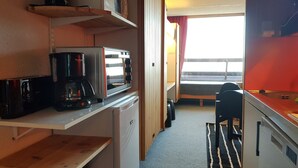 Una kitchenette compacta con microondas, cafetera y refrigerador pequeño.